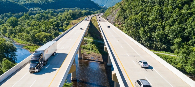 Trucks and cars driving down highway surrounded by green trees